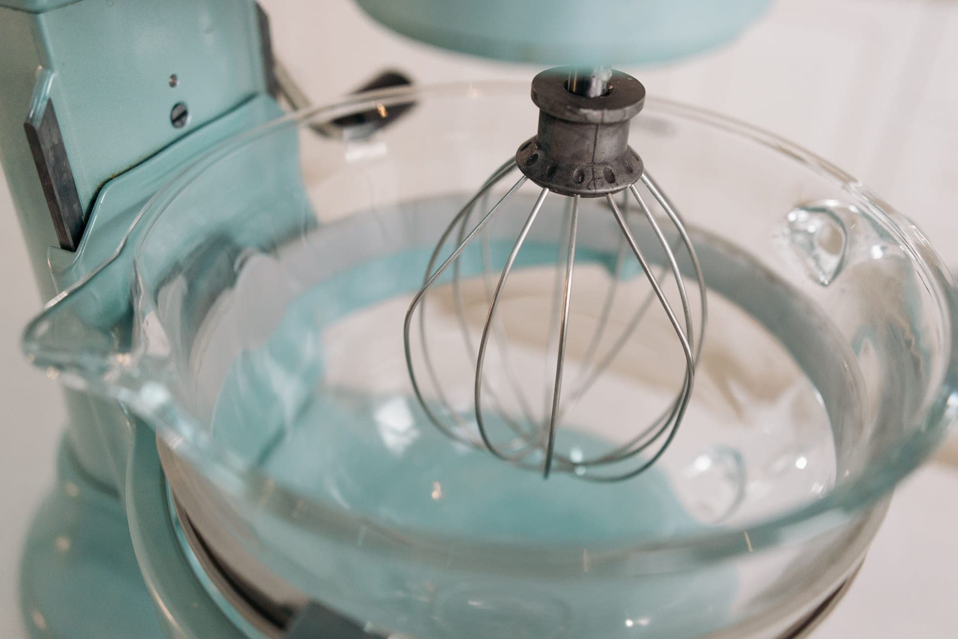A stand mixer fitted with a whisk attachment and a glass bowl