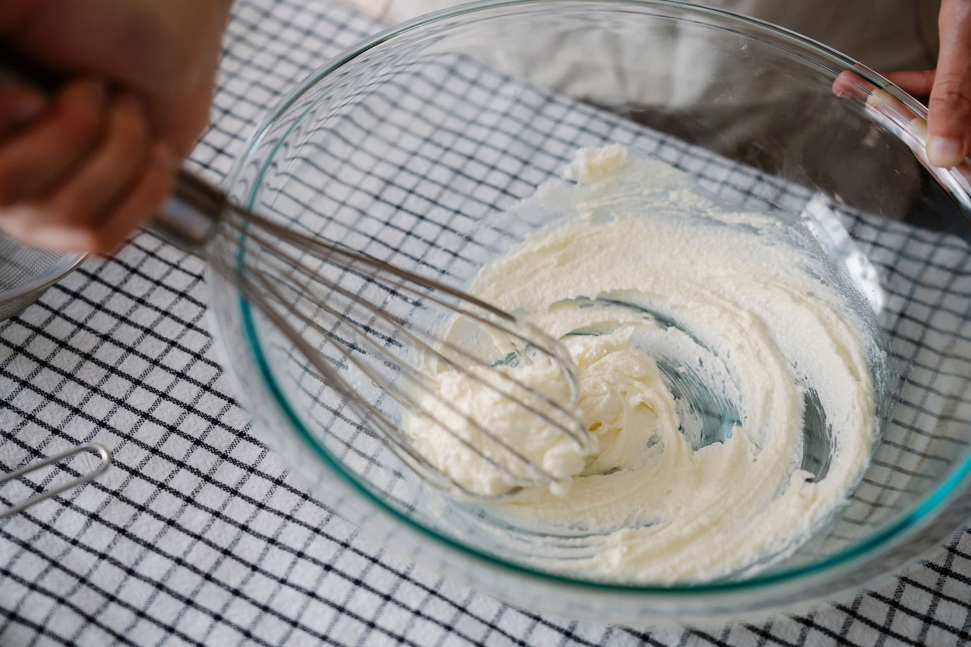 Cream being whisked by hand in a glass bowl